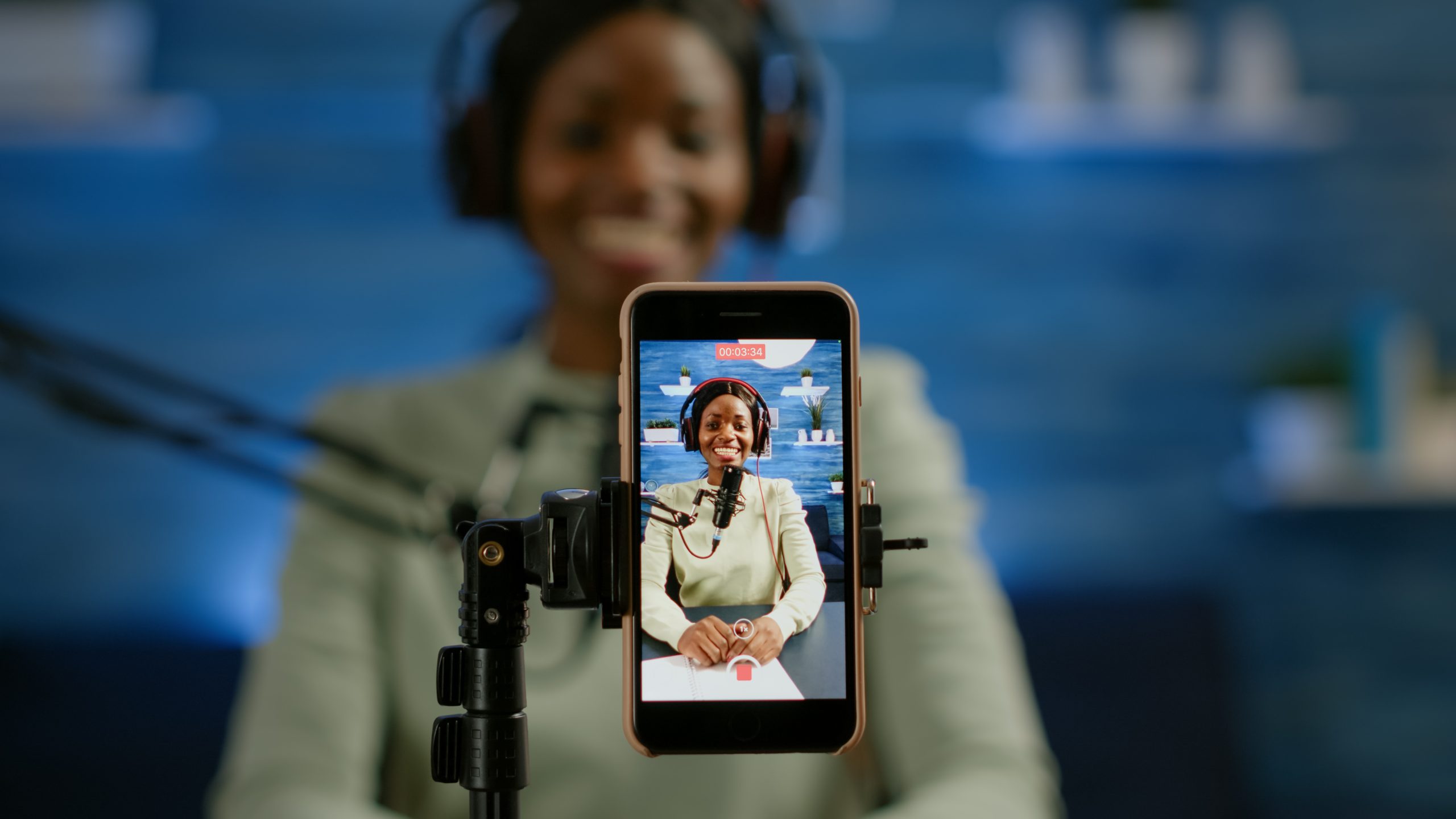 close up smartphone recording vlog african influencer home studio using smartphone speaking during livestreaming blogger discussing podcast wearing headphones professional microphone scaled